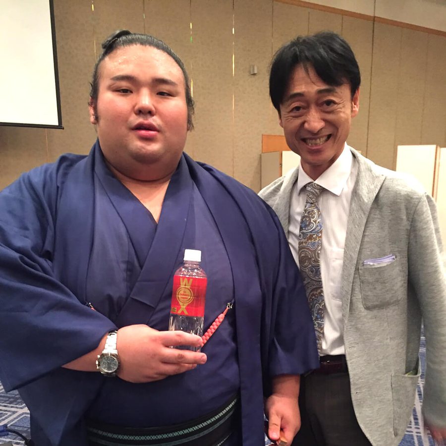 Sumo wrestler in formal kimono holding a bottle of WOX beside the company founder